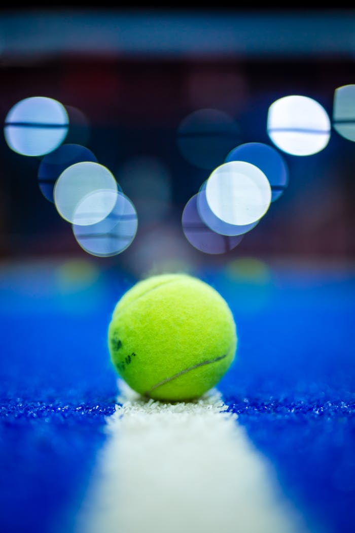 A vibrant close-up of a yellow tennis ball on a blue court under bokeh lights.